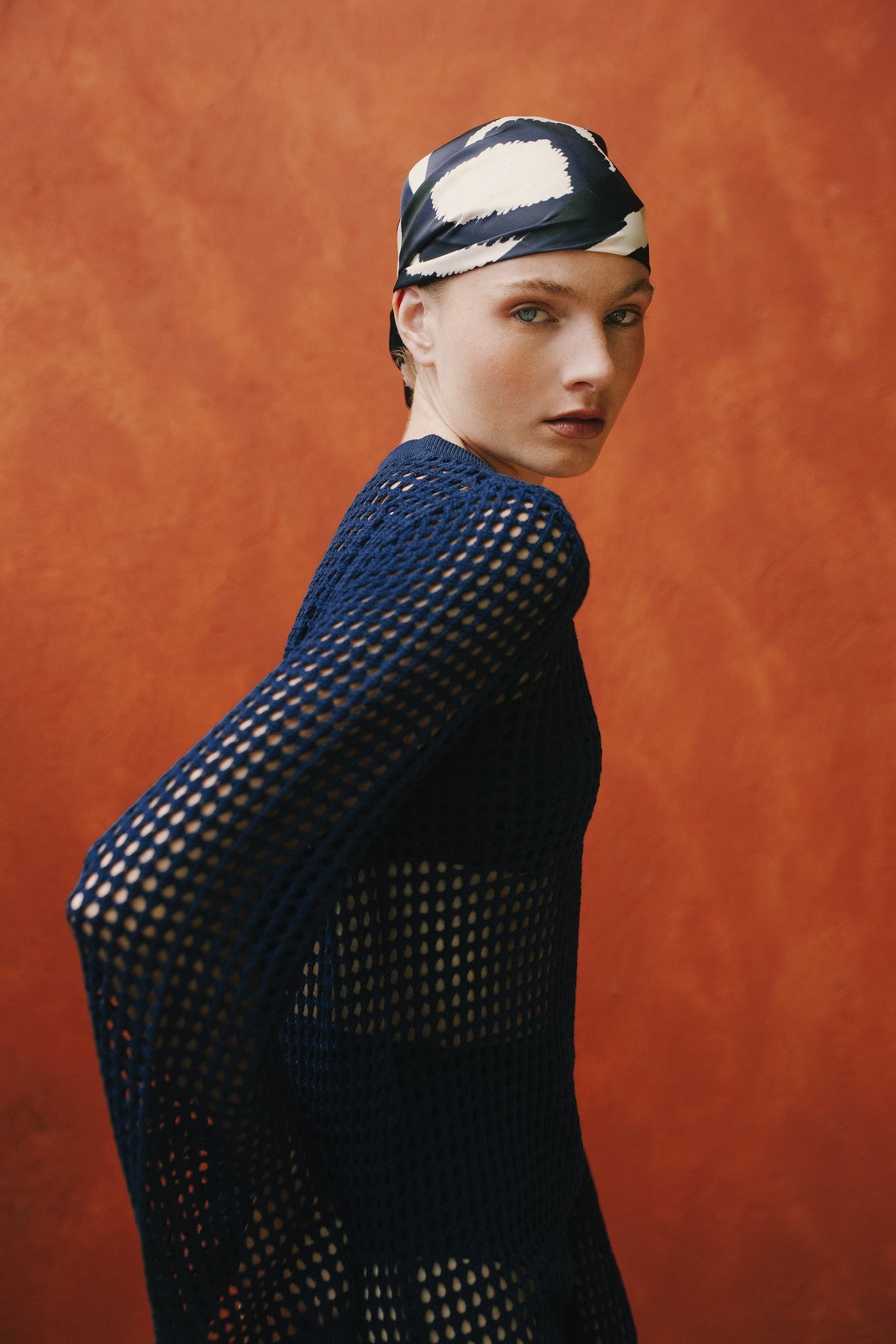 Editorial side shot of model in navy mesh dress against orange backdrop.