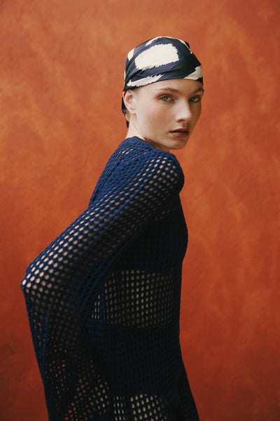 Editorial side shot of model in navy mesh dress against orange backdrop.