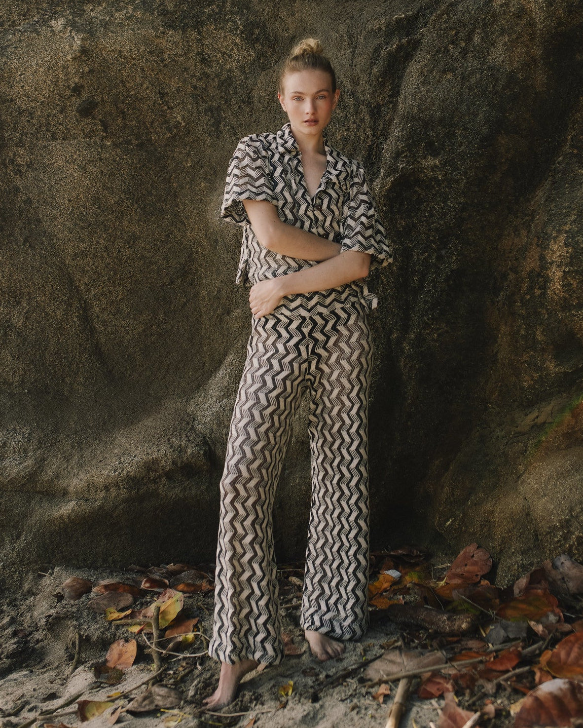 Person wearing a black and white patterned outfit standing in front of a large rock.