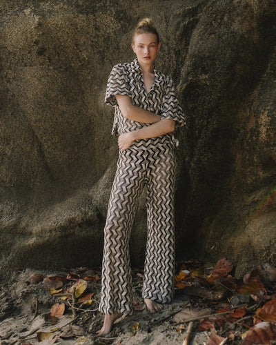 Person wearing a black and white patterned outfit standing in front of a large rock.