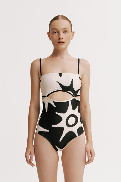 Model wearing a black and white abstract patterned swimsuit on a plain background