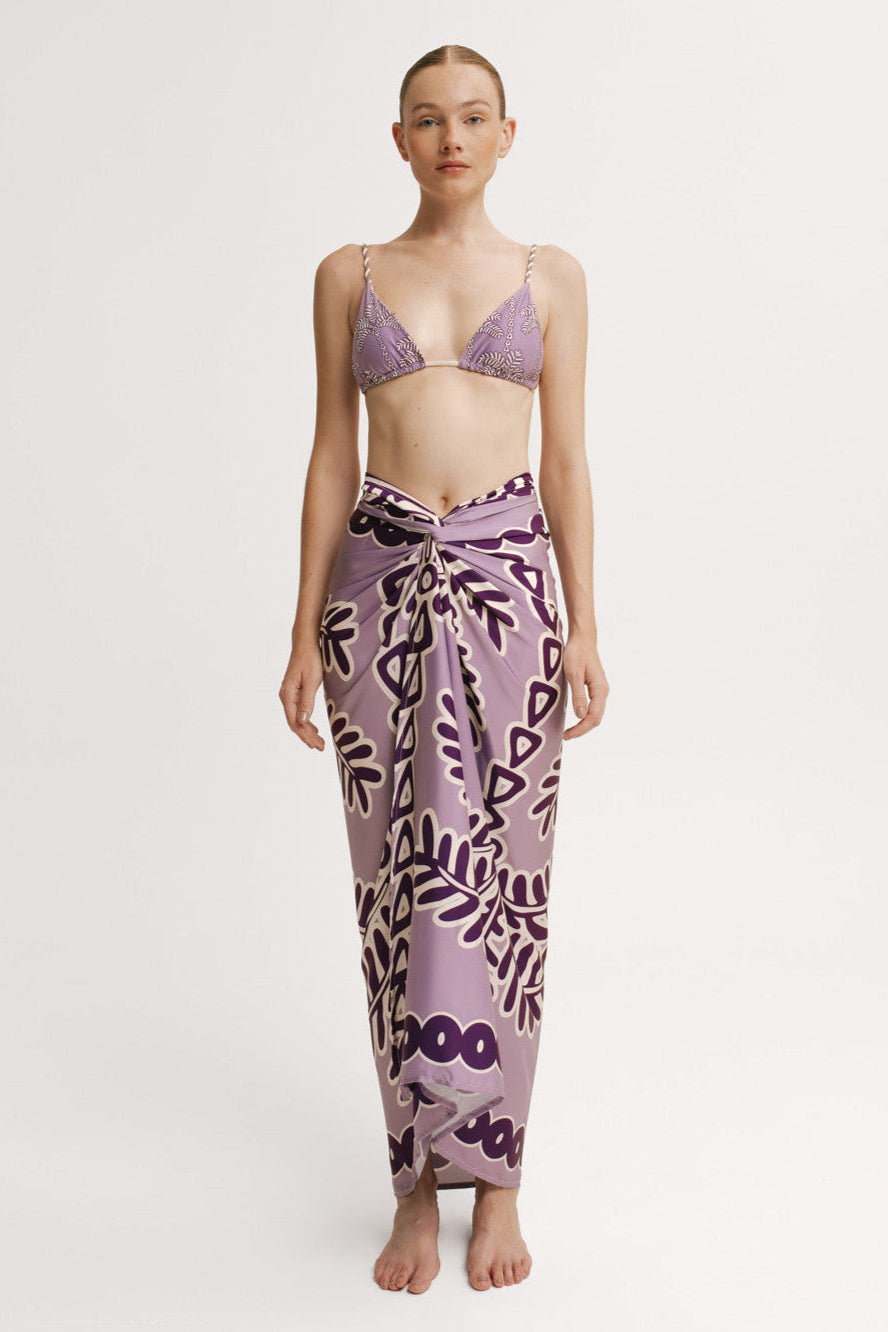 Woman wearing a purple patterned bikini and sarong on a white background