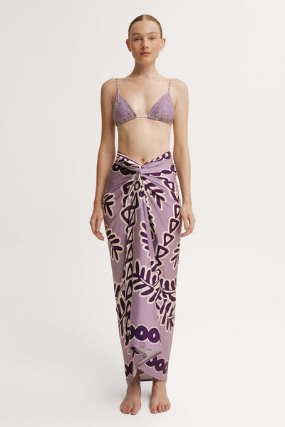 Woman wearing a purple patterned bikini and sarong on a white background