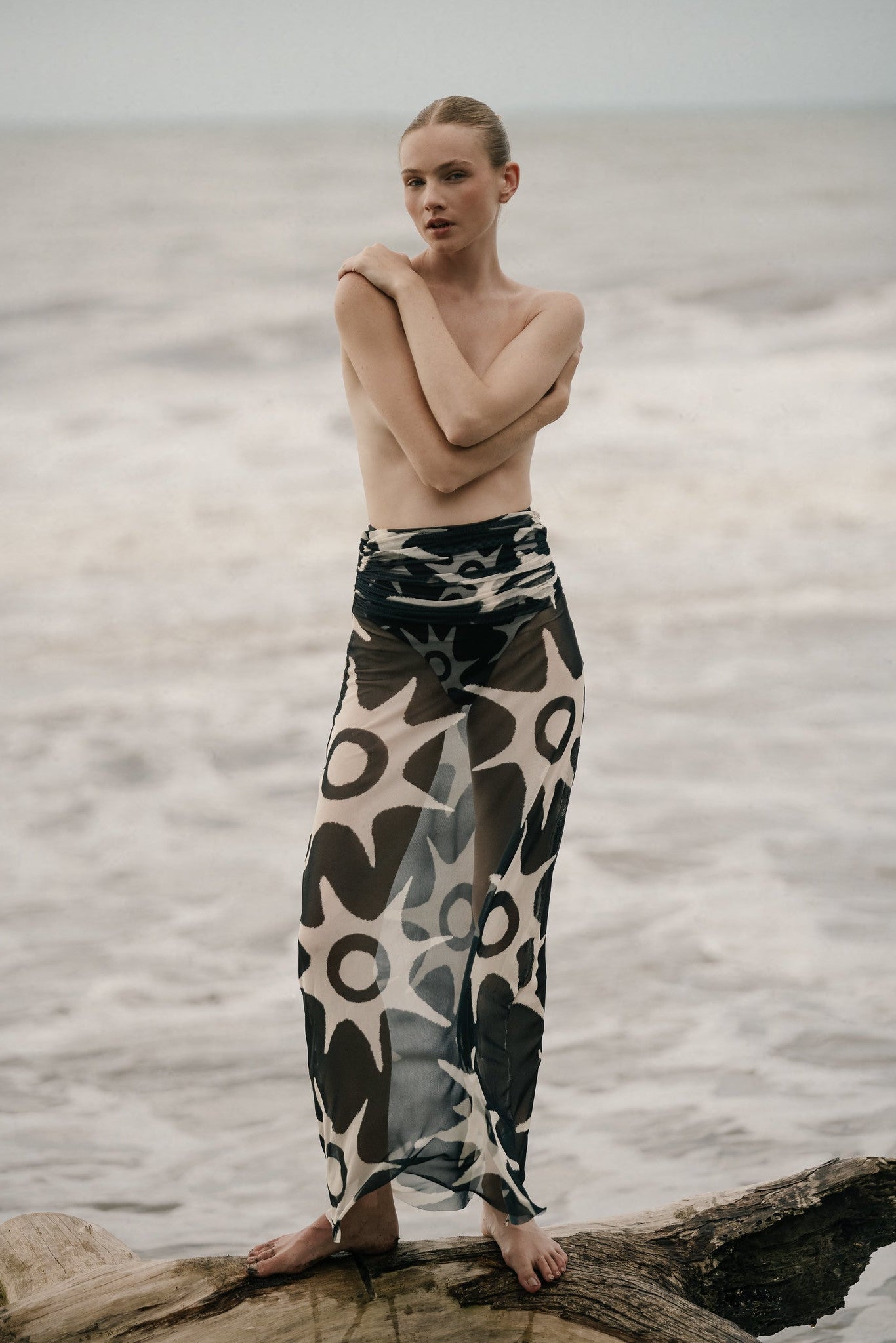 Model topless wearing a Skirt on the beach, showing the sheer solar-print mesh fabric and draped waistband.