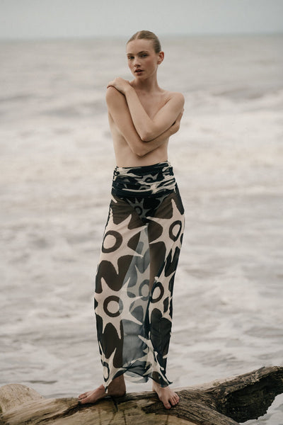 Model topless wearing a Skirt on the beach, showing the sheer solar-print mesh fabric and draped waistband.