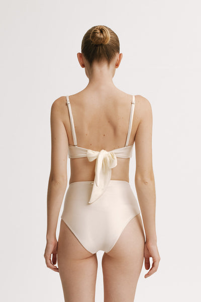 Woman wearing aN IVORY swimsuit with a bow detail on a white background