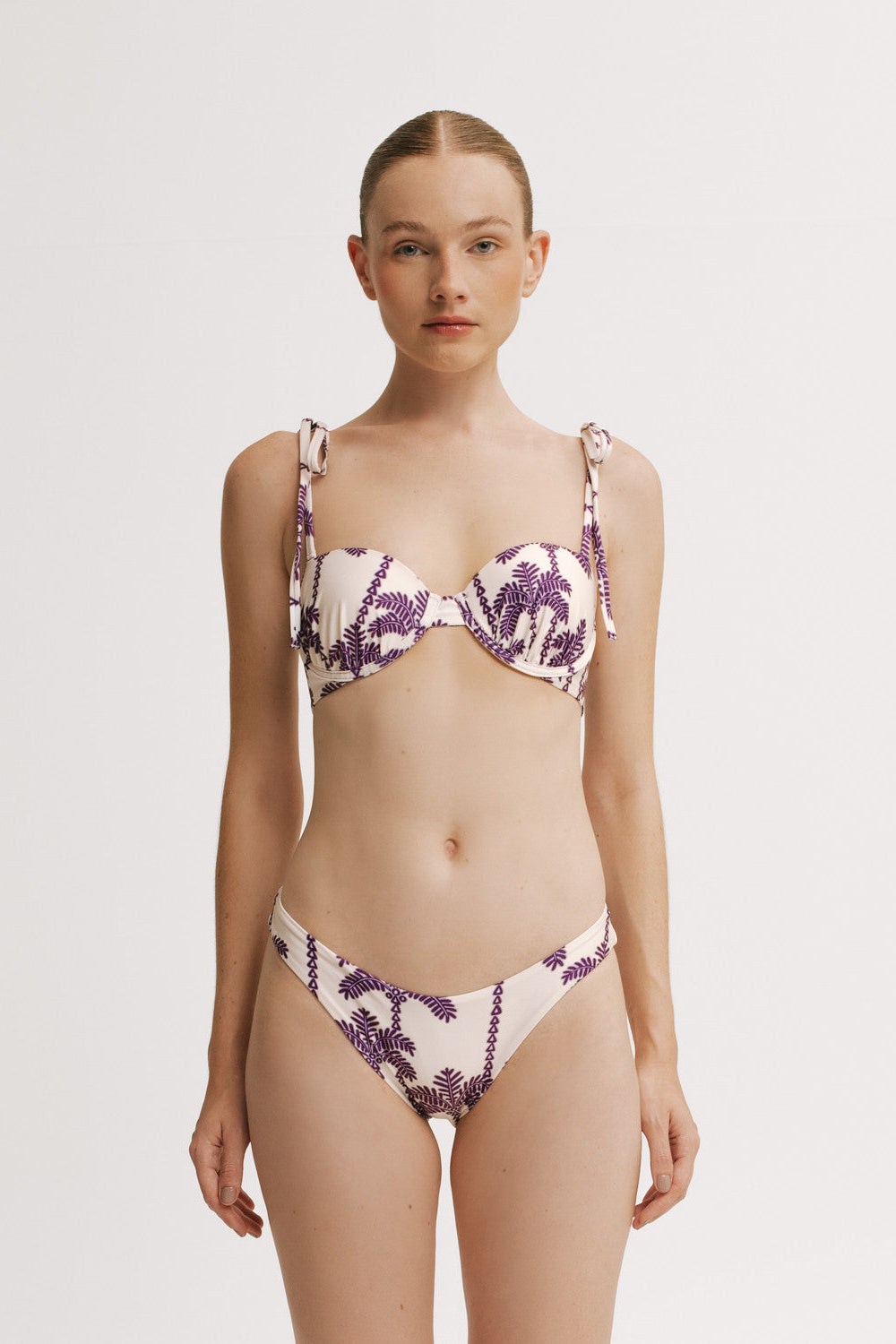 Woman wearing a palm print bikini set in purple and white on a plain background