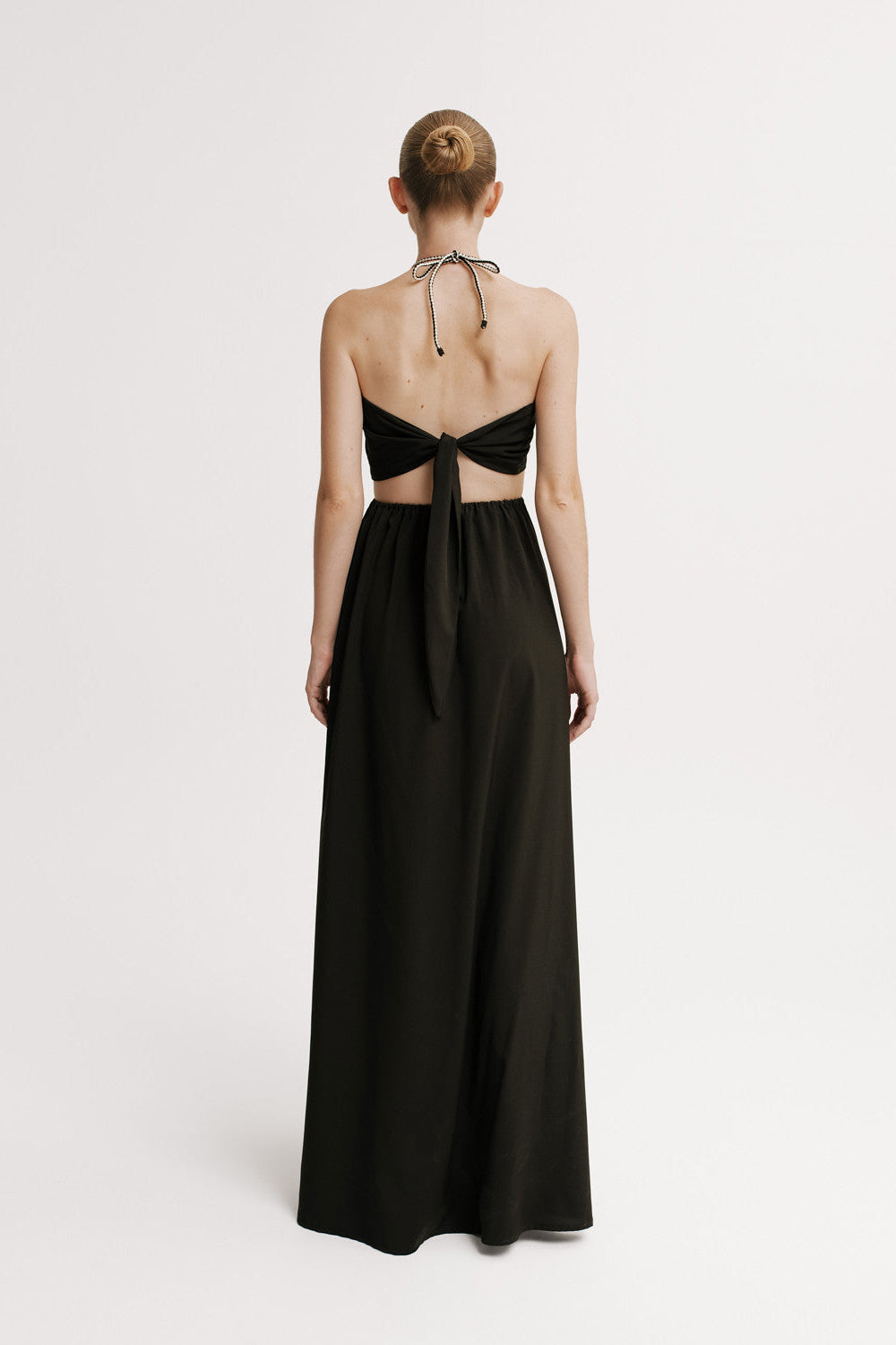 Model wearing a black evening gown with cut-out back design on a white background