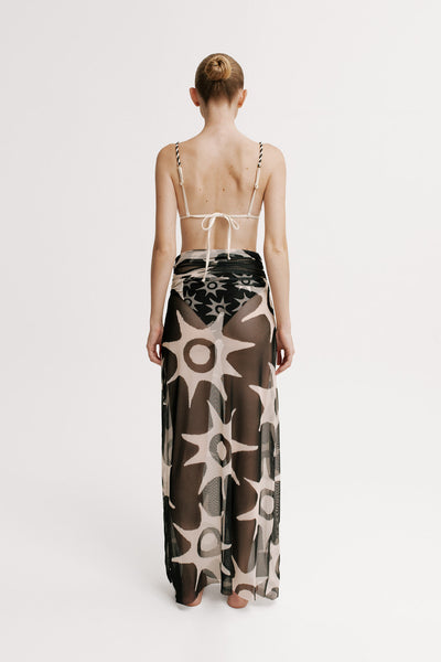 Model wearing a long, patterned dress with thin straps on a white background