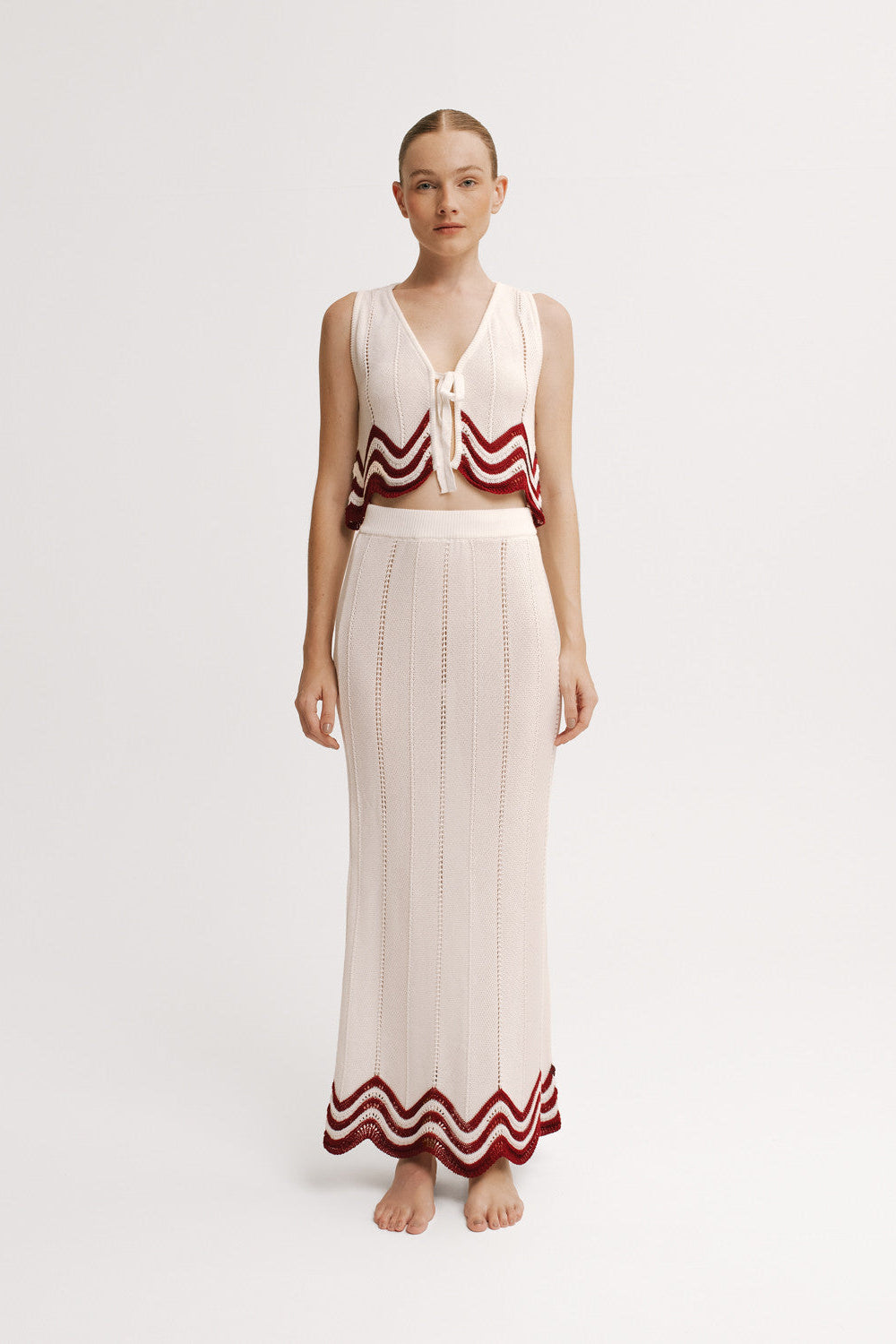 Woman wearing a sleeveless top and long skirt with red and white patterns on a white background