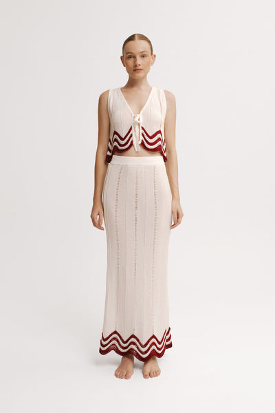 Woman wearing a sleeveless top and long skirt with red and white patterns on a white background