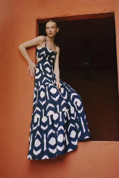 Woman in a blue and white patterned dress standing against an orange wall.