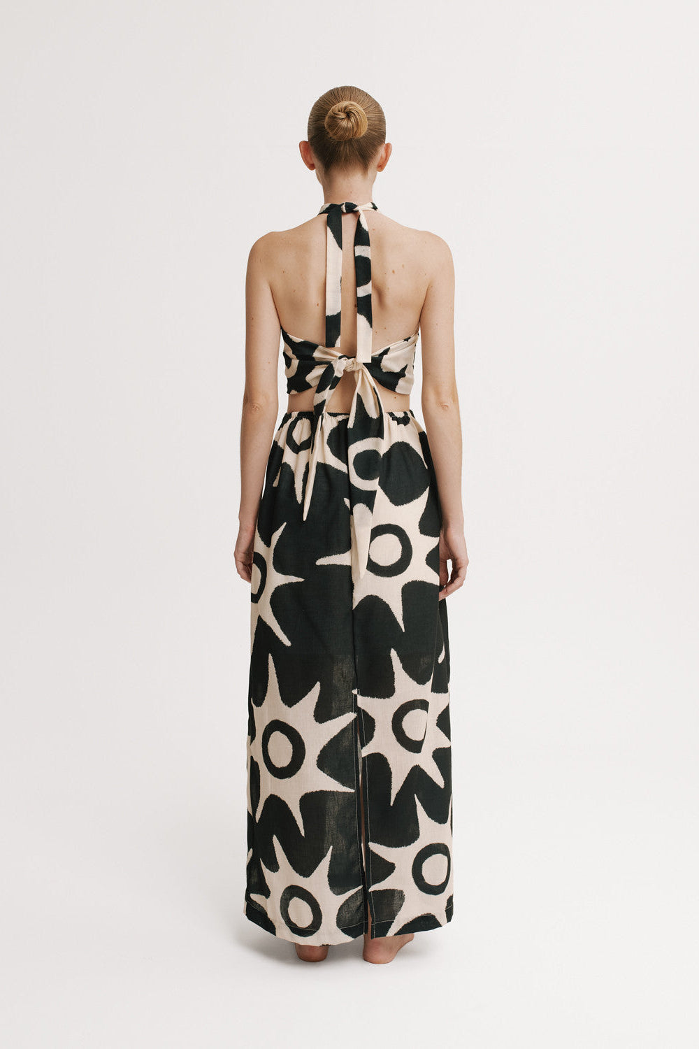 Model wearing a long, patterned dress with a halter neck design on a white background