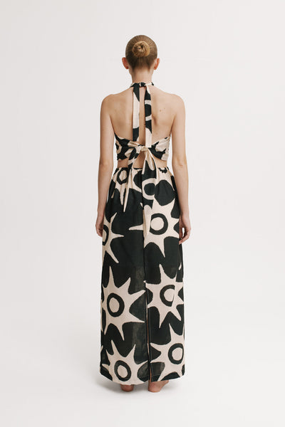 Model wearing a long, patterned dress with a halter neck design on a white background