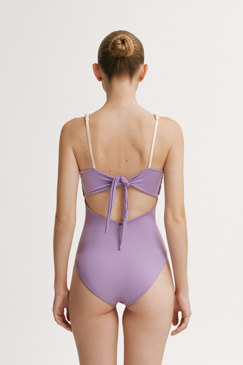 Purple one piece  swimsuit with open back worn by a model on a light gray background