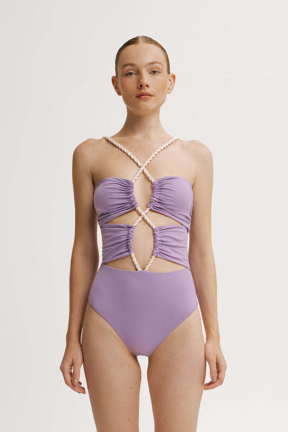 Woman wearing a criss-cross purple one piece swimsuit with a white background
