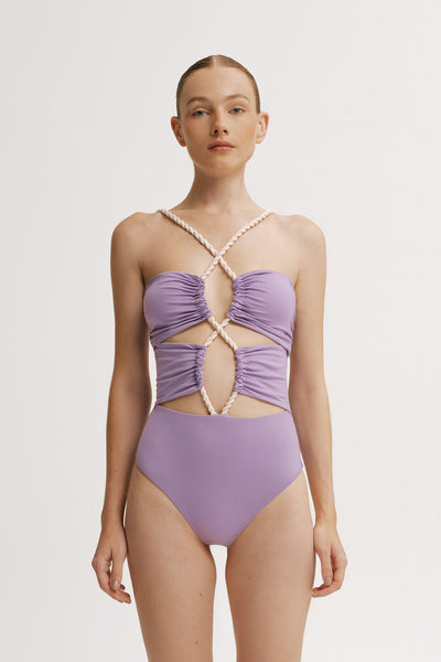 Woman wearing a criss-cross purple one piece swimsuit with a white background