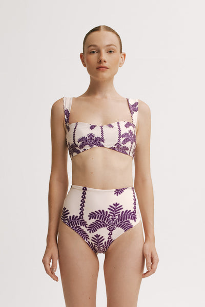 Woman wearing a white and purple palm patterned bikini set on a plain background