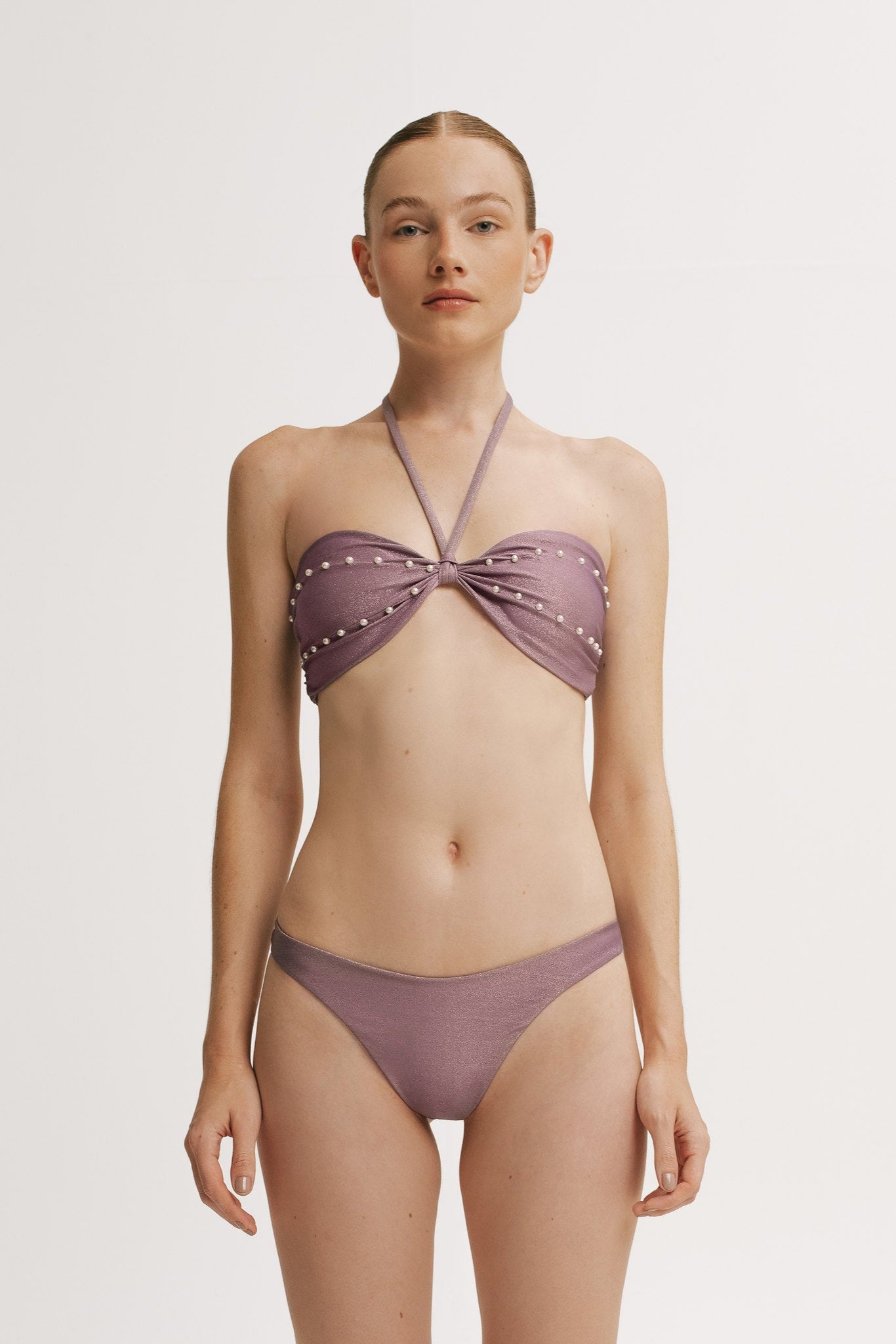 Woman wearing a purple bikini with studded details on a white background