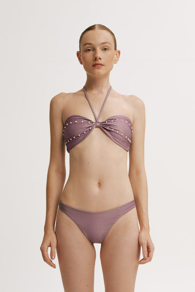 Woman wearing a purple bikini with studded details on a white background