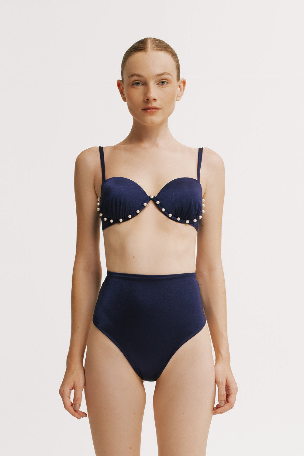 Woman wearing a navy blue bikini with polka dot details on a white background