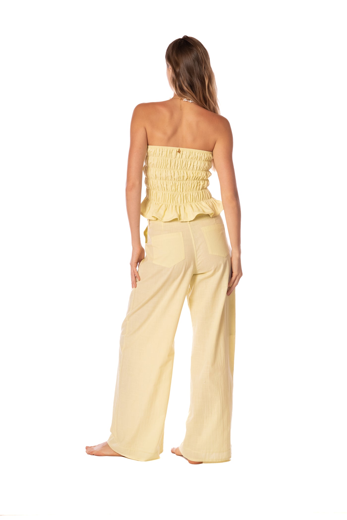 Woman wearing a yellow strapless top and wide-leg pants on a white background