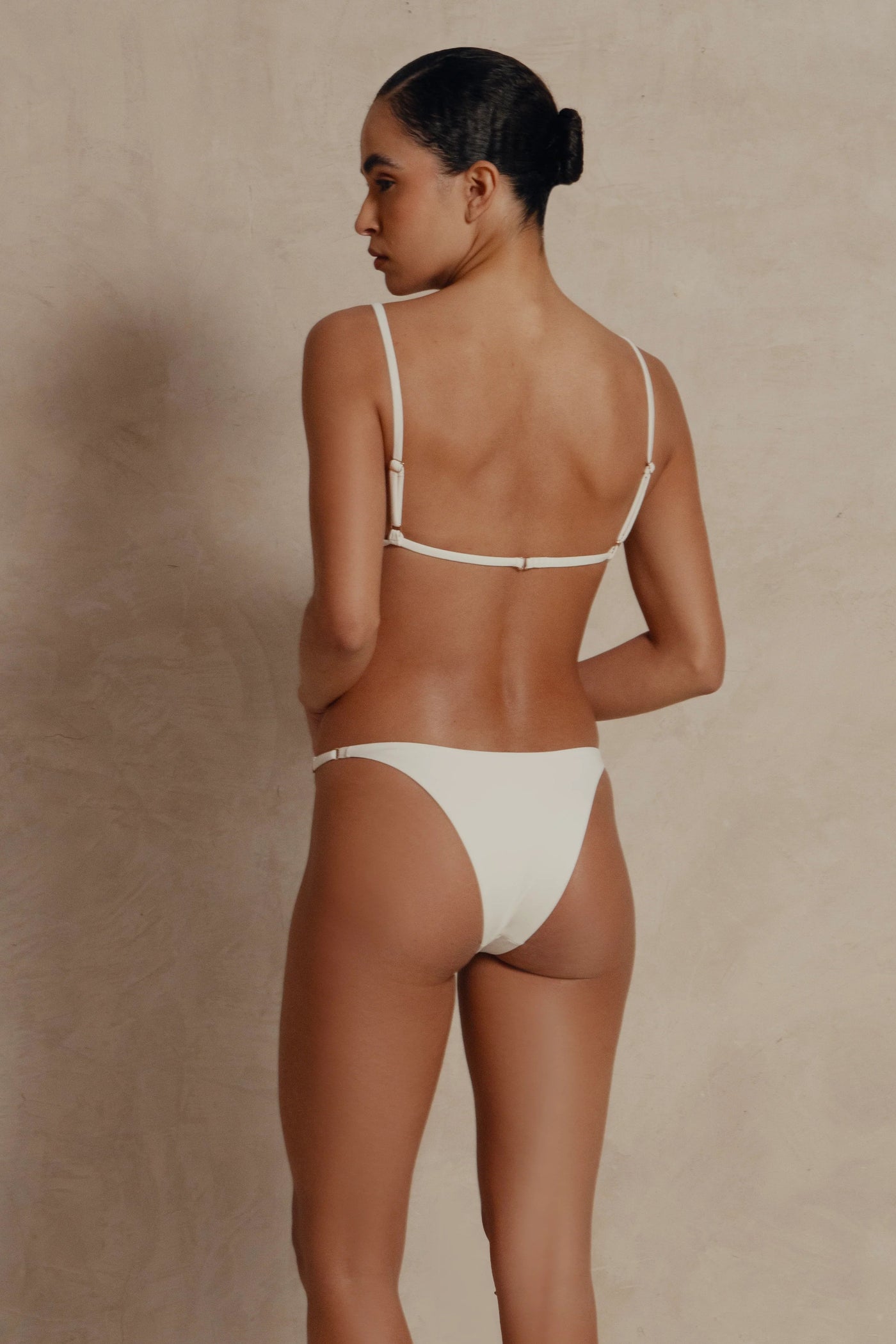 Woman wearing a white bikini against a beige background