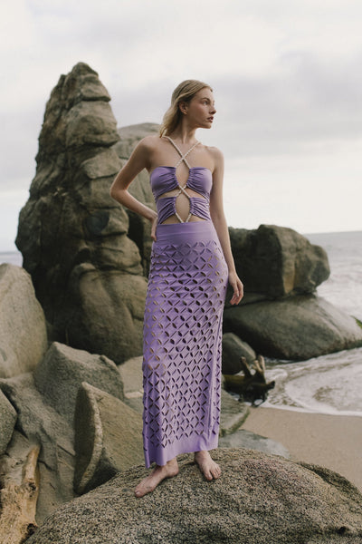 Woman in a purple dress standing on a rocky beach with ocean and sky in the background