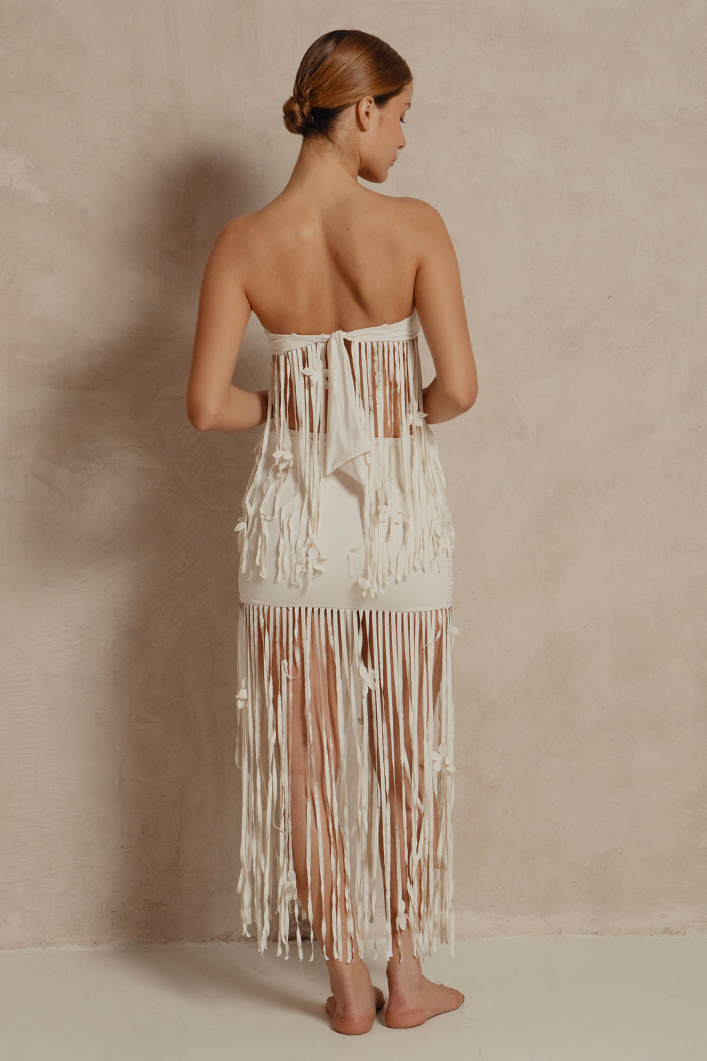 Woman wearing a strapless, fringed dress against a beige background