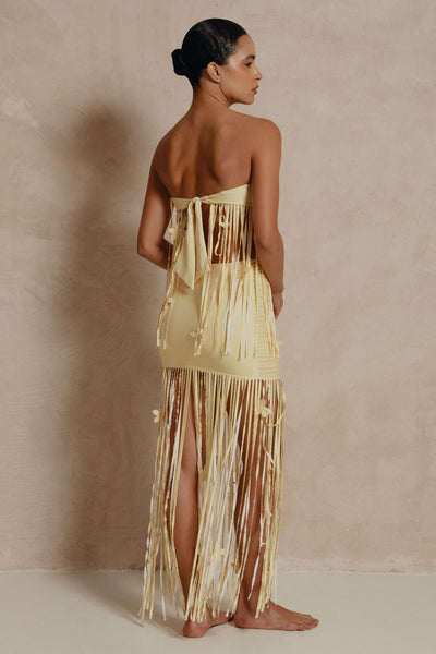 Woman wearing a strapless, long, fringed dress against a beige background