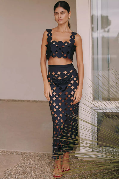 Woman wearing a laser-cut black matching set featuring a geometric crop top and high-waisted midi skirt, styled by WOAHCO – luxury resortwear fashion.